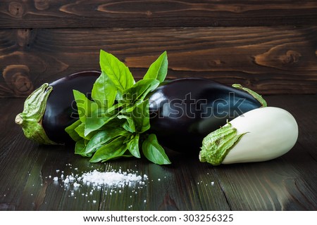 Purple and white eggplant (aubergine) with basil on dark wooden table. Fresh raw farm vegetables - harvest from the garden in rustic kitchen. Rural still life