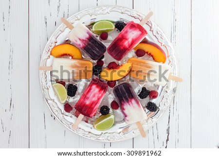 Colorful homemade popsicles with fresh fruits and berries on ice cubes in vintage silver tray