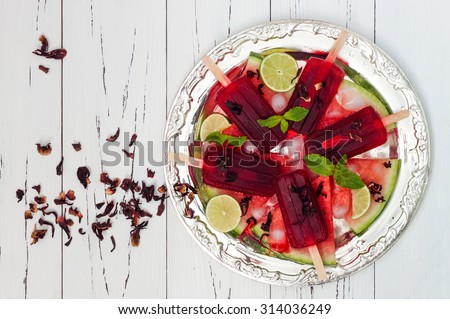 Refreshing mexican style ice pops - watermelon, hibiscus, lime paletas - popsicles, served on vintage silver tray with watermelon slices, lime, mint leaves. Top view, copy space. Cinco de Mayo recipe