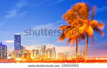 City of Miami Florida, night skyline palm trees and moving traffic. . Cityscape of residential and business buildings illuminated at sunset