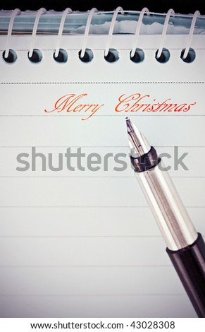 Vintage fountain pen writes holiday message on a notepad with red ink