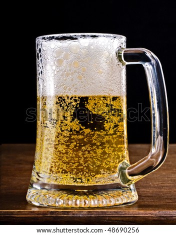 Fresh cold golden light beer with froth served in a glass pint mug on a wooden bar. Closeup shot on black background