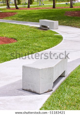 Modern concrete benches and path in a public park with green grass and trees on a beautiful spring day