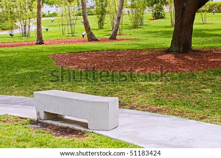 Modern concrete benches and path in a public park with green grass and trees on a beautiful spring day