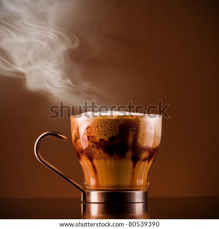 Closeup shot of Delicious smoking hot coffee drink macchiato, espresso with steamy milk and froth and added chocolate syrup for layered effect. Served on a bar in a glass cup. Textured background