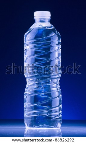 Drinking water in a plastic recyclable bottle, lit by cool light and with blue background. Closeup shot.