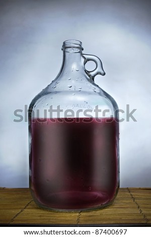 One gallon glass jug filled with wine, set on a table with blue background