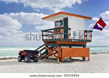 Summer scene with an orange colorful lifeguard house in a typical Art Deco style and a beach rescue car in Miami Beach, Florida with blue sky and ocean in the background.
