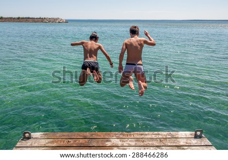 Summer vacation and the water safety. Two kids jump off the deck of lakeside cottage.