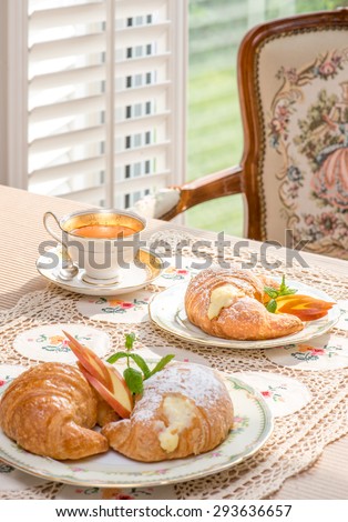 Retro / Vintage style tea room, vintage home interior, embroidery table cloth. Tea time. Antique teacup and furniture. Afternoon tea at home. Golden. Bright sunlight. Croissant with cream filling.