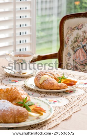 Retro / Vintage style tea room, vintage home interior, embroidery table cloth. Tea time. Antique teacup and furniture. Afternoon tea at home. Golden. Bright sunlight. Croissant with cream filling.