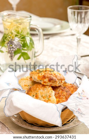 English tea biscuits in basket on a summer time dinner table. Bouquet in vintage English vase. Bird shaped napkin rings. In bright natural light. Herbal tea in vintage jar.