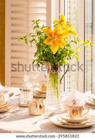 Summer time dinner table setting Tablescaping. Bouquet in vintage Italian Wine decant. Afternoon tea. Warm late afternoon sunlight. Antique English teacups and plates from 1940s.