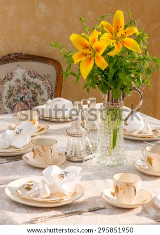 Summer time dinner table setting Tablescaping. Bouquet in vintage Italian Wine decant. Bird shaped napkin rings. Warm late afternoon sunlight. Antique English teacups and plates from 1940s.