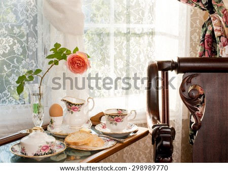 Breakfast - room service.. Vintage / antique style interior design. Matching patterns of tableware and the curtain. Fine bone china, antique rocker chair. Landscape orientation.