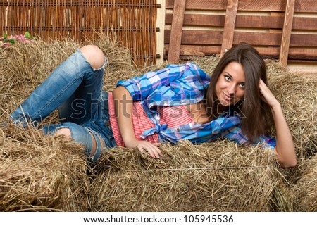 Portrait of brunette girl in a plaid shirt. Young woman in costume of cowboy lies on haystack