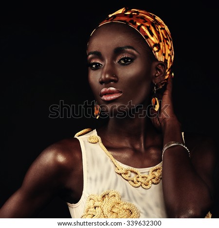 African-american fashion style. Beautiful African woman wearing headscarf and gold bathing suit handmade looking at camera while standing against black background.