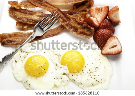 Close up view of breakfast including bacon and eggs with strawberries.