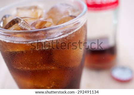 Glass of iced soft drink with the bottle and the lid in the background