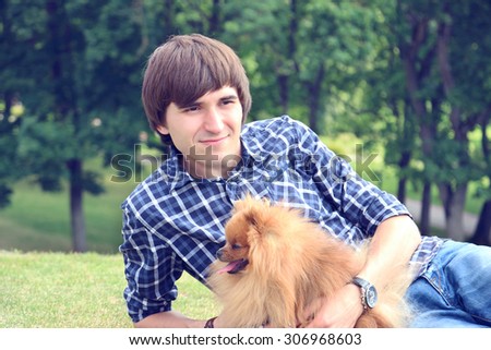 Handsome happy man with cute pomeranian dog lying on the green grass. Man and his lovely dog. Love of animals. Dog man\'s best friend
