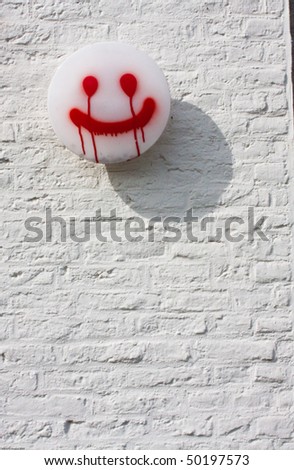 Spray painted happy face on a white lamp on a white brick wall