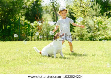Happy kid and pet dog playing with soap bubbles at backyard lawn