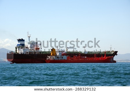 A chemical tanker which is anchored being refueled by a fuel barge at sea