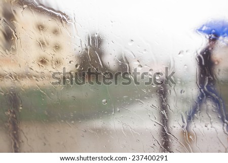 blurred background image with blurred rain drops and man with umbrella hurrying in the rain