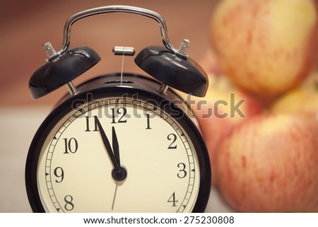 alarm clock showing almost twelve o\'clock with red and yellow apples on the background. extreme closeup