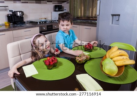 Two happy preschool children who eat healthy strawberry in the kitchen