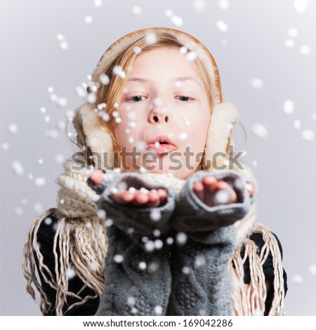 cute little girl in warm hat and gloves blowing snow on white background