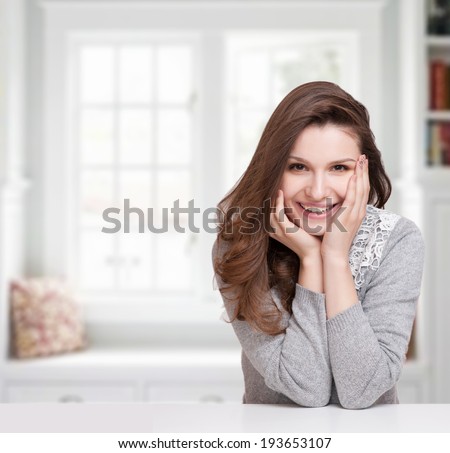Close up portrait of a happy smiling woman resting her chin on her hands and looking directly at the camera