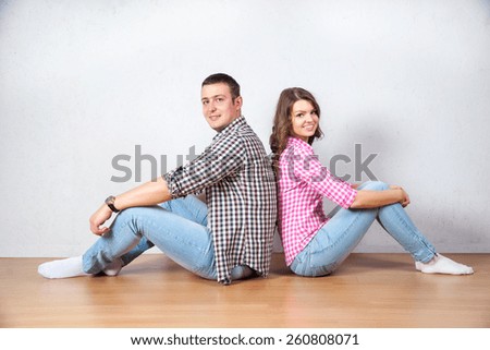 Young couple relaxing on the floor at home sitting barefoot back to back each looking up into the air with a thoughtful smile as they plan their future together
