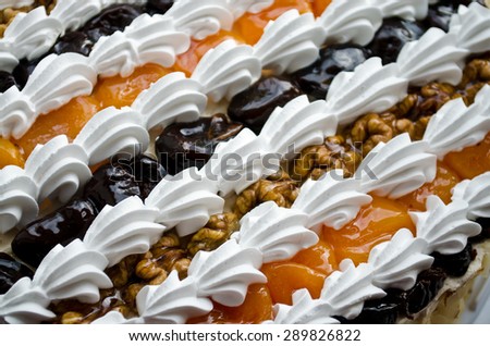 Fruit cake with dried apricots and prunes, decorated with cream and nuts.