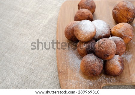 Freshly baked cheese donuts with powdered sugar on a chopping board.