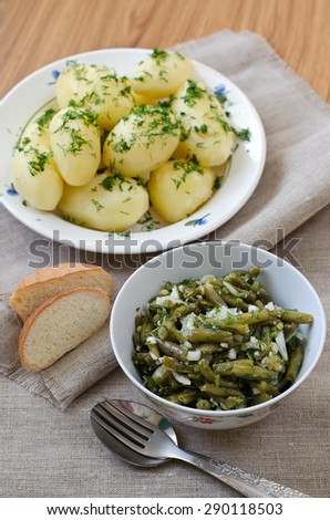 Marinated green beans with onions, garlic, dill. Cooked with olive oil. In the background a bowl with boiled potatoes