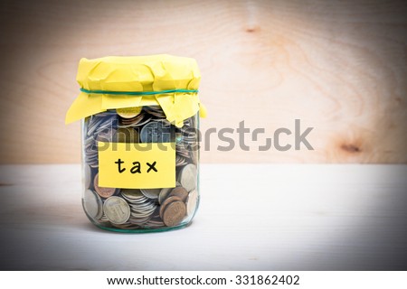 Financial concept. Coins in glass money jar with tax label. Wooden background