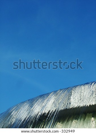 Water spilling over concrete fountain against bright blue sky