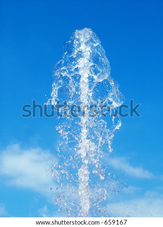 Clear water spout against bright blue sky - spurt of water is in soft focus