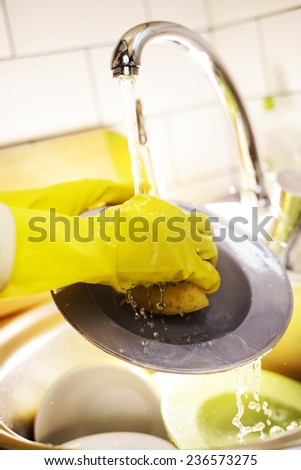 Man washes the dishes in the kitchen in yellow gloves