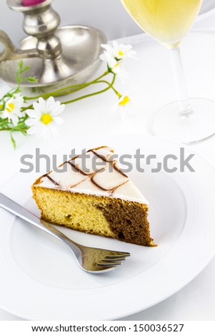 Cake and silver fork on a white plate with flowers, candle holder and glass of juice in background
