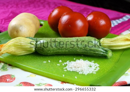 Zucchini, tomatoes and rice ingredients on green chopping board.
