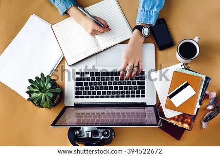stylish young girl working  analytics holding pen on craft background with laptop and papers flat lay
