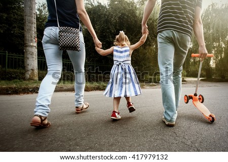 happy stylish parents holding hands with daughter and walking in sunny  street, amazing family moment