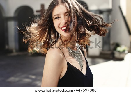 happy stylish woman waving hair in sunlight at old european city street, luxury look, space for text, moment of carefree and true happiness