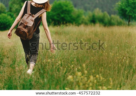 stylish hipster woman walking in grass and holding  in hand herb  wildflowers  in summer mountains, travel concept, peaceful relaxing moment
