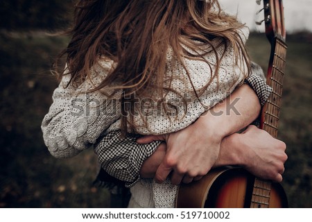 man with guitar hugging his boho gypsy woman closeup in windy field. atmospheric sensual moment. stylish hipster couple in fashionable look. rustic wedding concept