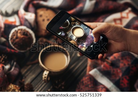 hand holding phone taking photo of stylish winter flat lay coffee cookies and spices on wooden rustic background. cozy mood autumn. instagram blogging workshop concept.
