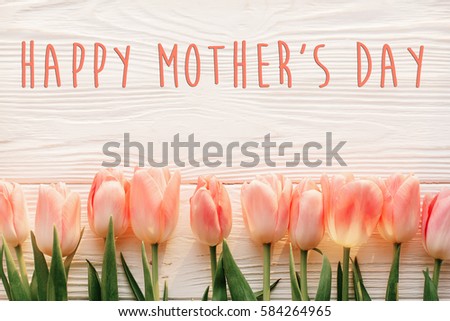 happy mother\'s day text sign on pink tulips on white rustic wooden background. greeting card concept. sensual tender women image. spring flowers flat lay