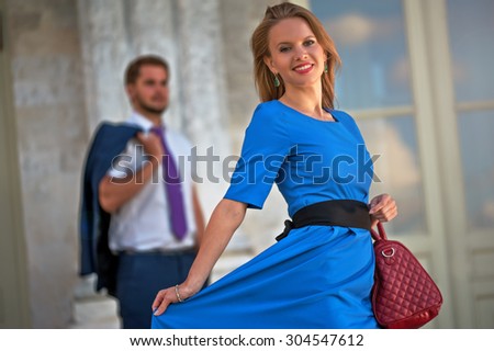 Young beautiful woman in a blue dress and a red handbag standing in front of a man